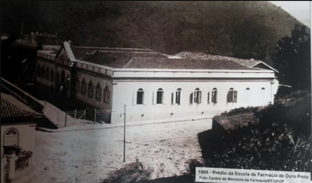 Foto antiga e em preto e branco do prédio da Escola de Farmácia de Ouro Preto, em Minas Gerais. Ele é quadrado e tem diversas janelas em formato arredondado em suas laterais.
