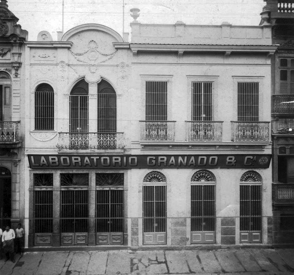Foto antiga e em preto e branco da fachada do Laboratório Granado, no Rio de Janeiro. Um prédio de 2 andares, diversas janelas e o nome do estabelecimento escrito em um letreiro. 