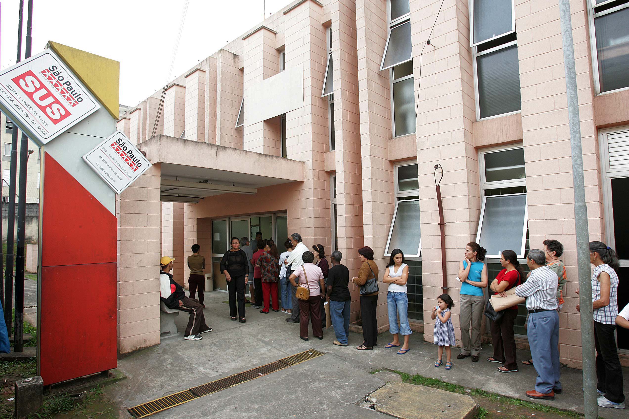 Foto de uma fila de pessoas em pé no lado de fora de um hospital.