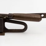Foto de um objeto de metal e madeira conhecido como corta raízes. Ele tem uma base reta com uma alavanca com uma lâmina cortante em cima.