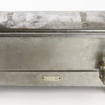 Foto de um equipamento antigo de esterilização de agulhas e seringas no formato de uma caixa metálica.