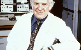 Foto do cientista Sir James Black posando e sorrindo. Ele é um homem branco de cabelos grisalhos e veste um jaleco branco.