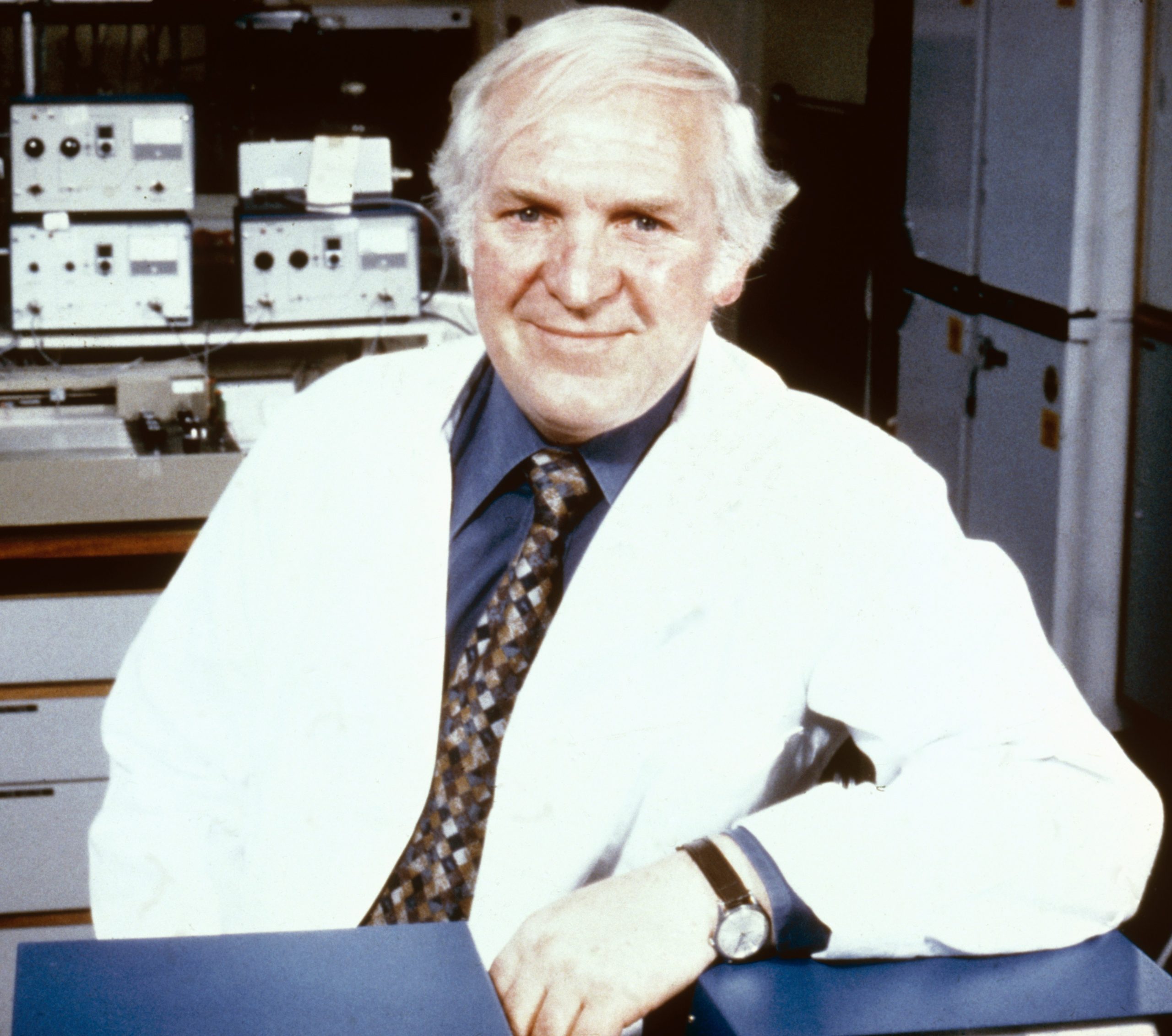 Foto do cientista Sir James Black posando e sorrindo. Ele é um homem branco de cabelos grisalhos e veste um jaleco branco.