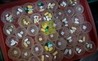 Foto de uma bandeja cheia de potes pequenos e transparentes contendo medicamentos de tamanhos e cores variados.