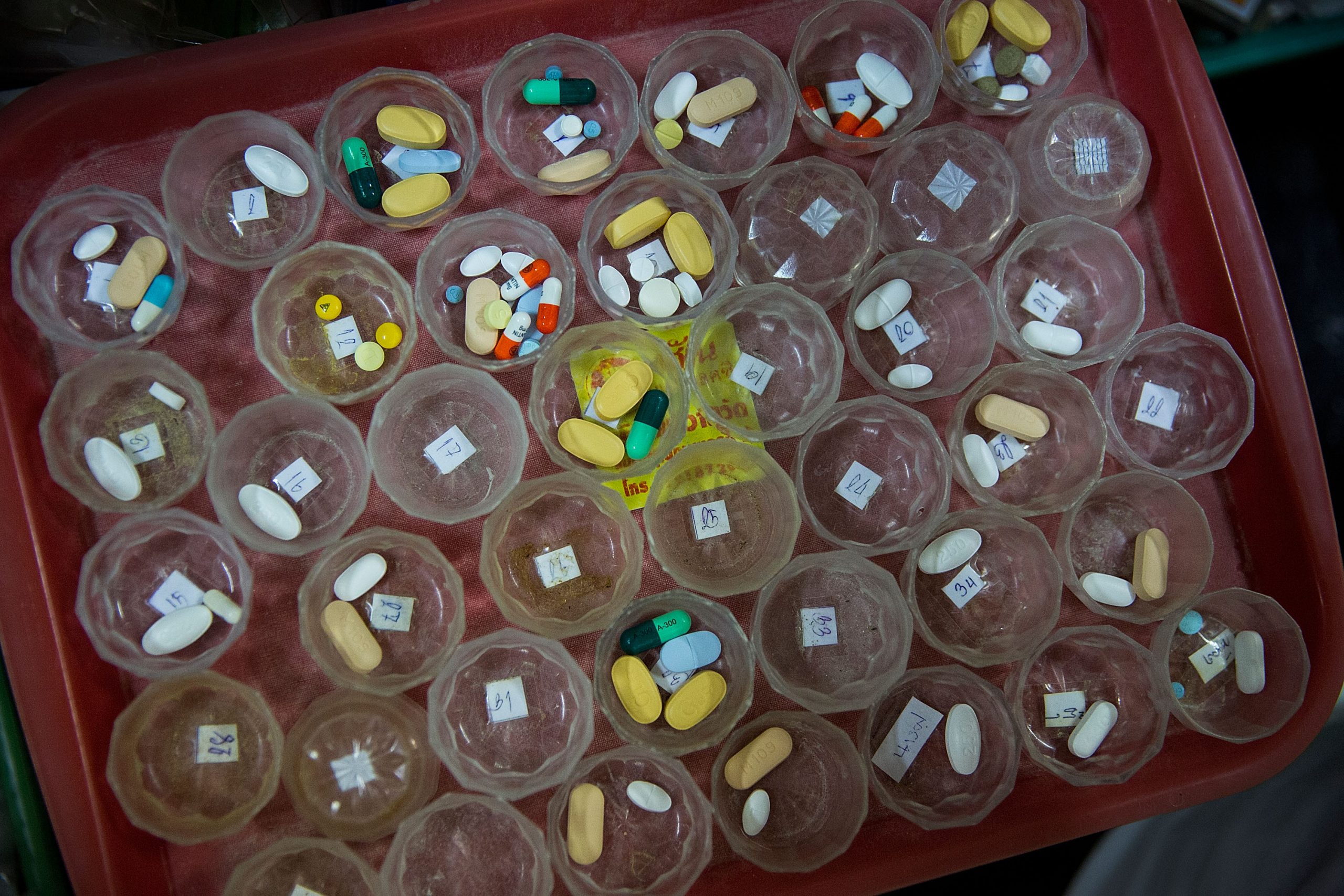 Foto de uma bandeja cheia de potes pequenos e transparentes contendo medicamentos de tamanhos e cores variados.