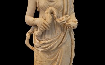 Estátua do deusa Hígia Asclépio. Ela está de pé e segura uma cobra em suas mãos.