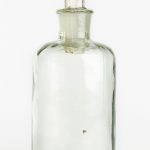 Foto de um frasco de vidro incolor com boca estreita e base arredondada.