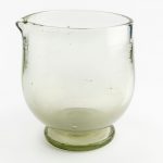 Foto de um gral de  vidro, objeto como um copo, com uma pequena curvatura tipo bico em uma das extremidades.