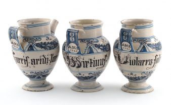 Foto de três jarras italianas da primeira metade do século 18, com pinturas em azul e escrita em preto.