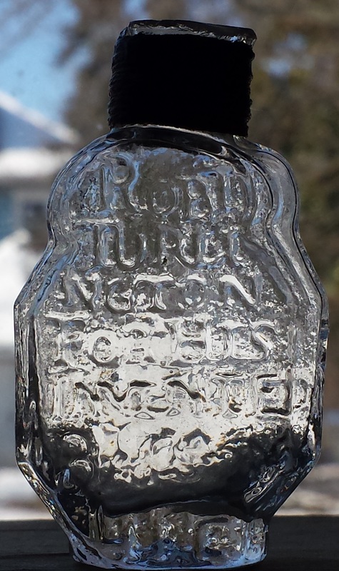Foto da garrafa do bálsamo de Turlington, de 1754. Uma garrafa de vidro com escritas em alto relevo.
