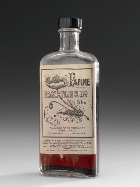 Foto de garrafa de vidro com um líquido vermelho, rótulo com flor desenhada e o texto: “Papine. Battle & Co. St. Louis”.