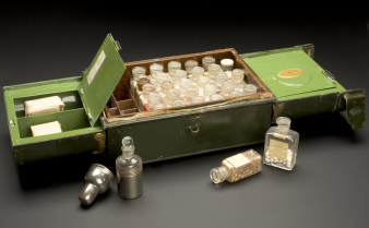 Foto de uma caixa antiga de ferro de medicamentos com vários frascos de vidros e substâncias diversas dentro deles.