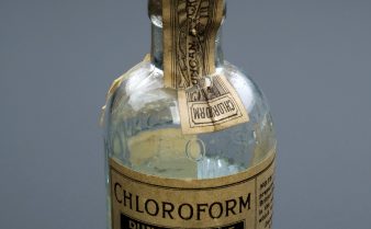 Foto de uma garrafa pequena com clorofórmio e com o rótulo amarelado pelo tempo.