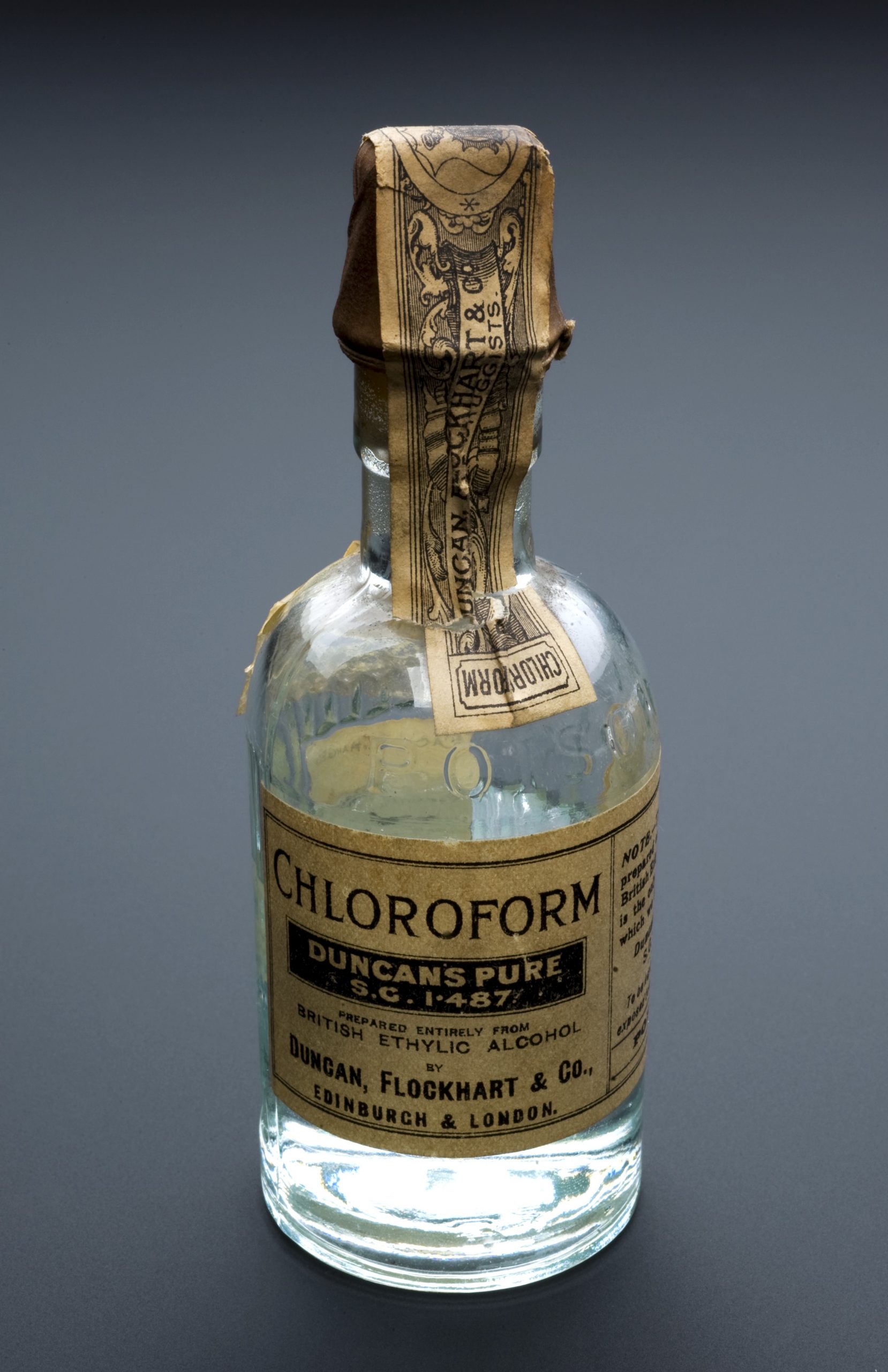 Foto de uma garrafa pequena com clorofórmio e com o rótulo amarelado pelo tempo.