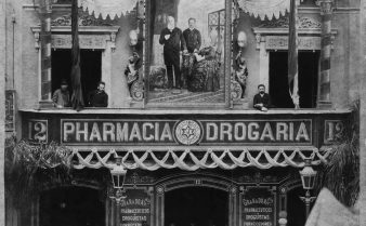 Foto em preto e branco da fachada da farmácia Granado em 1888. No andar superior, há uma sacada com duas portas e um quadro entre elas. Já no térreo, há três portas e várias pessoas na frente.