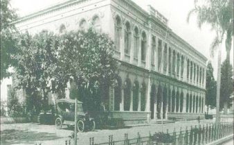 Foto em preto e branco da fachada do prédio da Faculdade de Farmácia e Odontologia de São Paulo, na década de 30. O prédio tem uma arquitetura de tendência art déco. Nas laterais da construção, há árvores, um carro estacionado na lateral, e uma cerca de ferro na parte da frente.