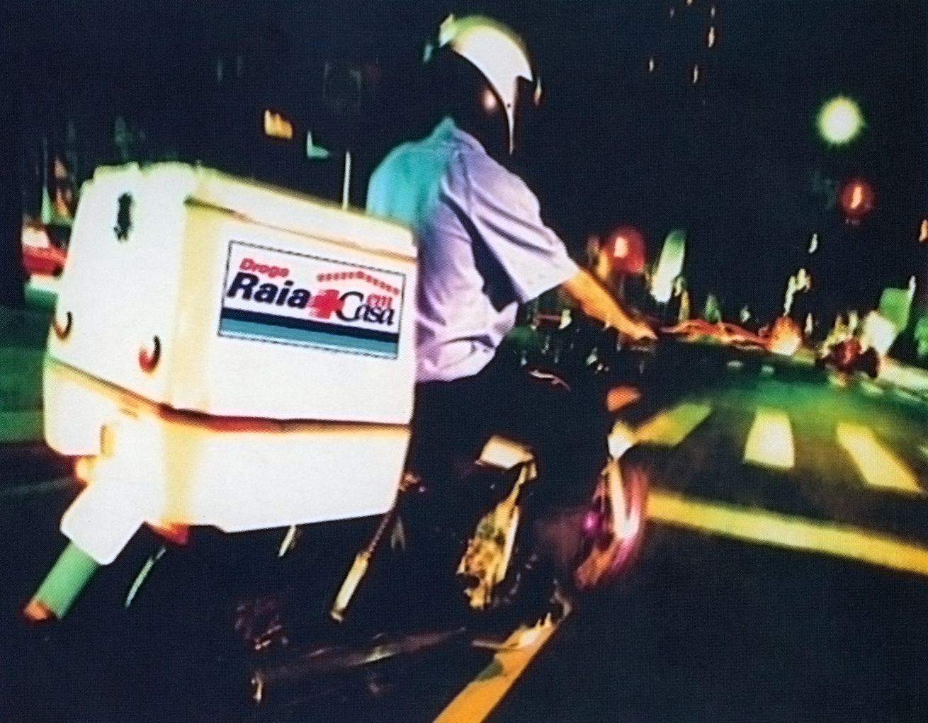 Foto de uma pessoa com capacete dirigindo uma moto de entrega de remédios da Droga Raia.