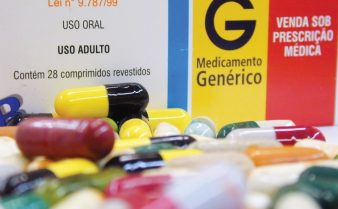 Foto com inúmeras pílulas coloridas espalhadas em frente à uma caixa de medicamento genérico.