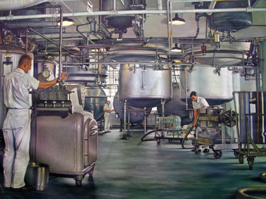 Foto interna de um galpão da indústrica química, com tambores metalizados para produtos químicos e outros equipamentos enormes. Há duas pessoas pessoas trabalhando, usando vestimentas brancas.